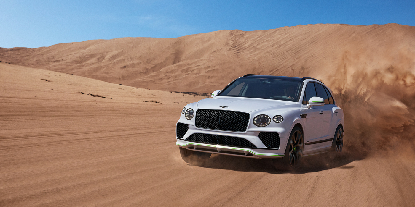 Bentley Manchester Bentley Bentayga Speed SUV front three quarter in Snow Quarts Pearlescent by Mulliner white paint driving dynamically through the desert