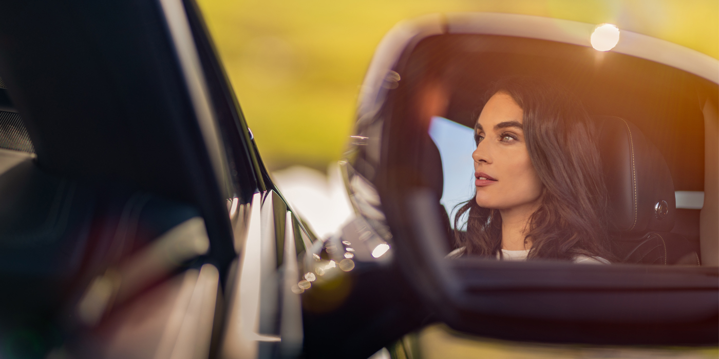 Bentley Manchester profile of dark haired woman's face in mirror of Bentley car in sunlight