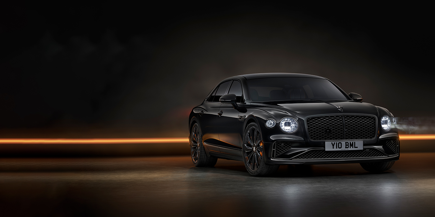 Bentley Manchester Bentley Flying Spur Black Edition sedan in Black Crystal paint against a dark grey and copper coloured background