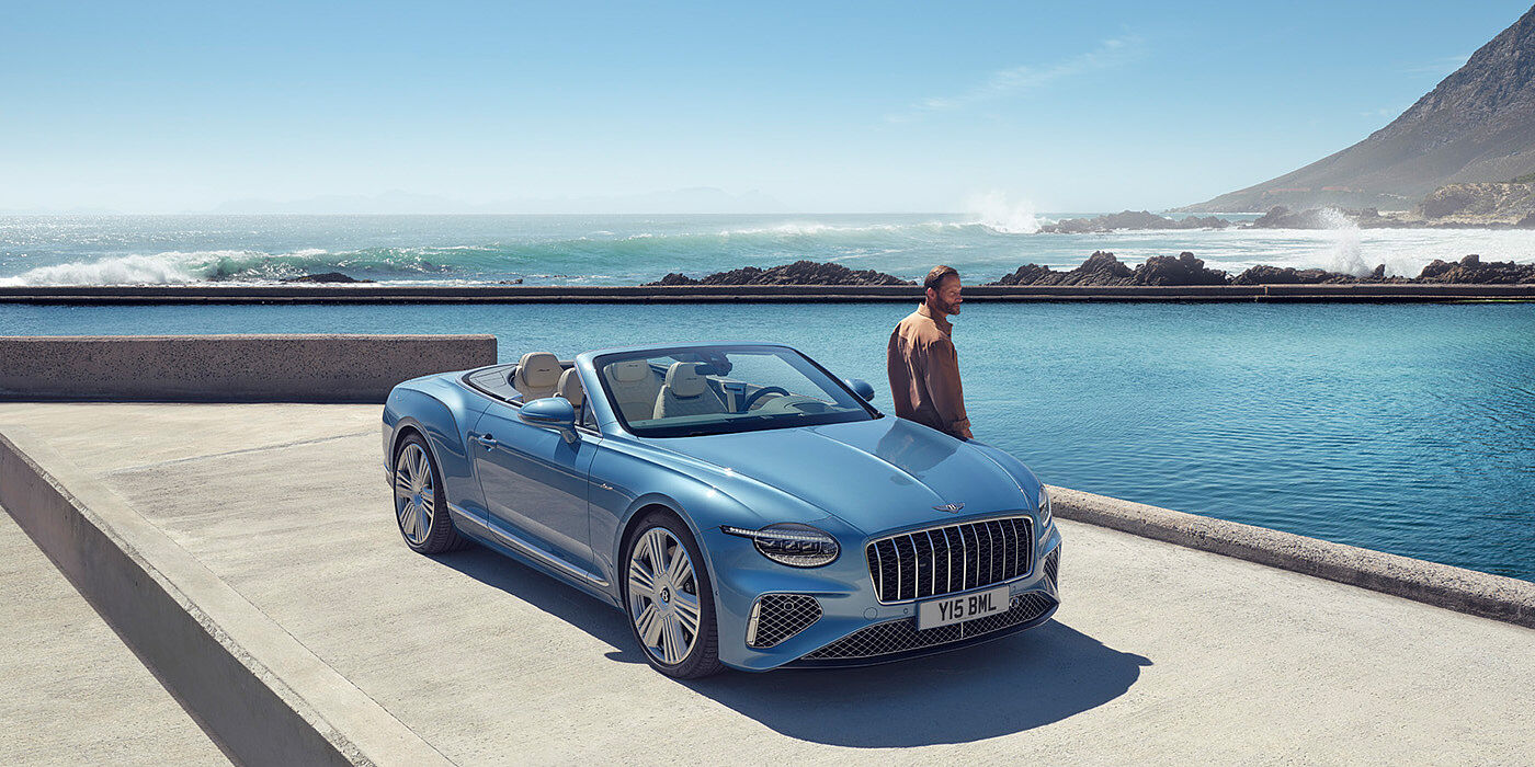 Bentley Manchester New Bentley Continental GTC Azure convertible front view in Light Windsor blue paint with 22 inch ten spoke wheels parked by the sea in the sunshine
