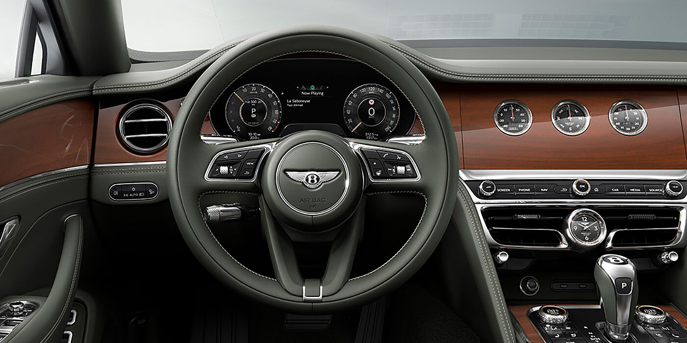 Bentley Manchester New Bentley Flying Spur sedan front cabin in Cumbrian Green hide and Crown Cut walnut veneer showing steering wheel and Rotating Display with three clocks on face