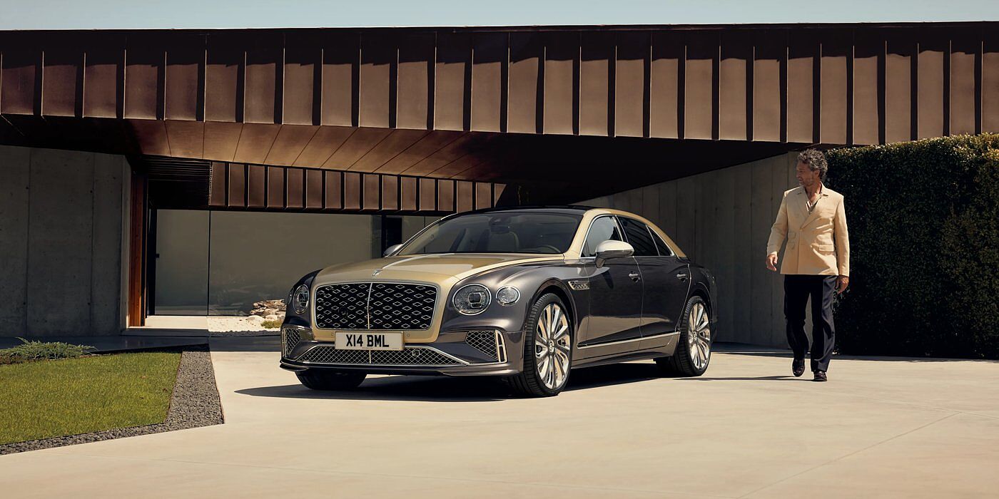 Bentley Manchester Bentley New Flying Spur Mulliner V8 hybrid sedan front three quarters in Rose Gold over Magnetic paint, parked near modern home