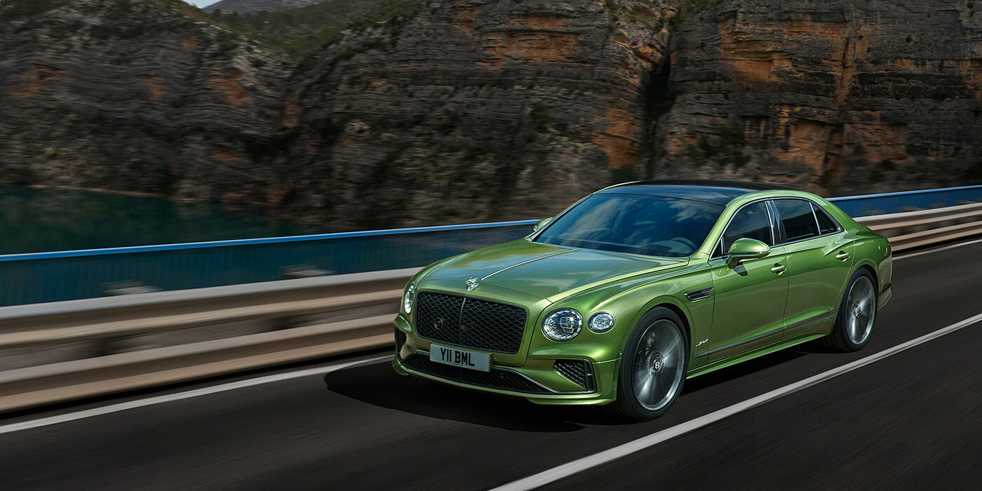 Bentley Manchester Bentley New Flying Spur Speed v8 hybrid sedan driving dynamically on a mountain road in Tourmaline Green paint