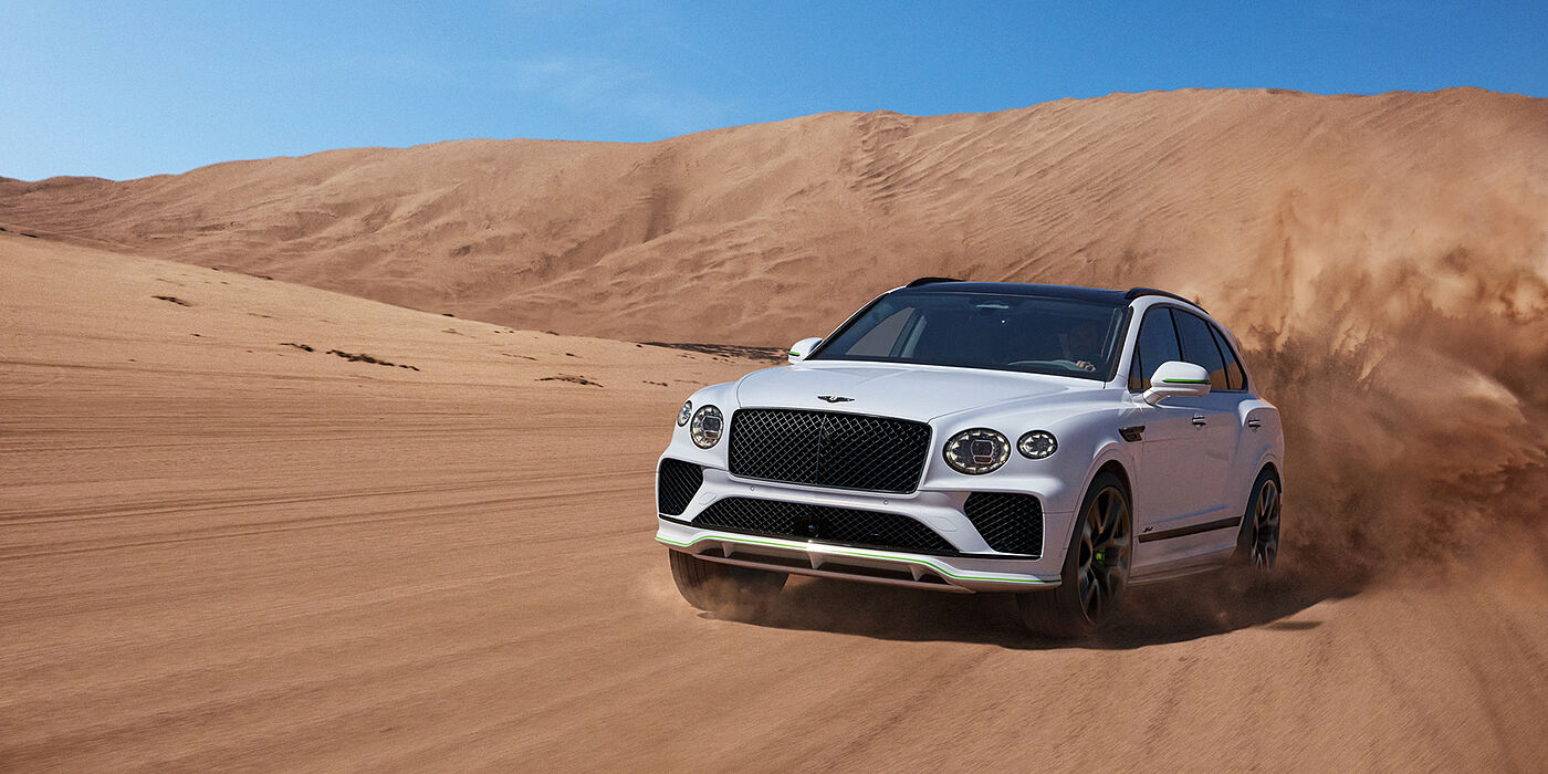 Bentley Manchester Bentley Bentayga Speed SUV front three quarter in Snow Quarts Pearlescent by Mulliner white paint driving dynamically through the desert