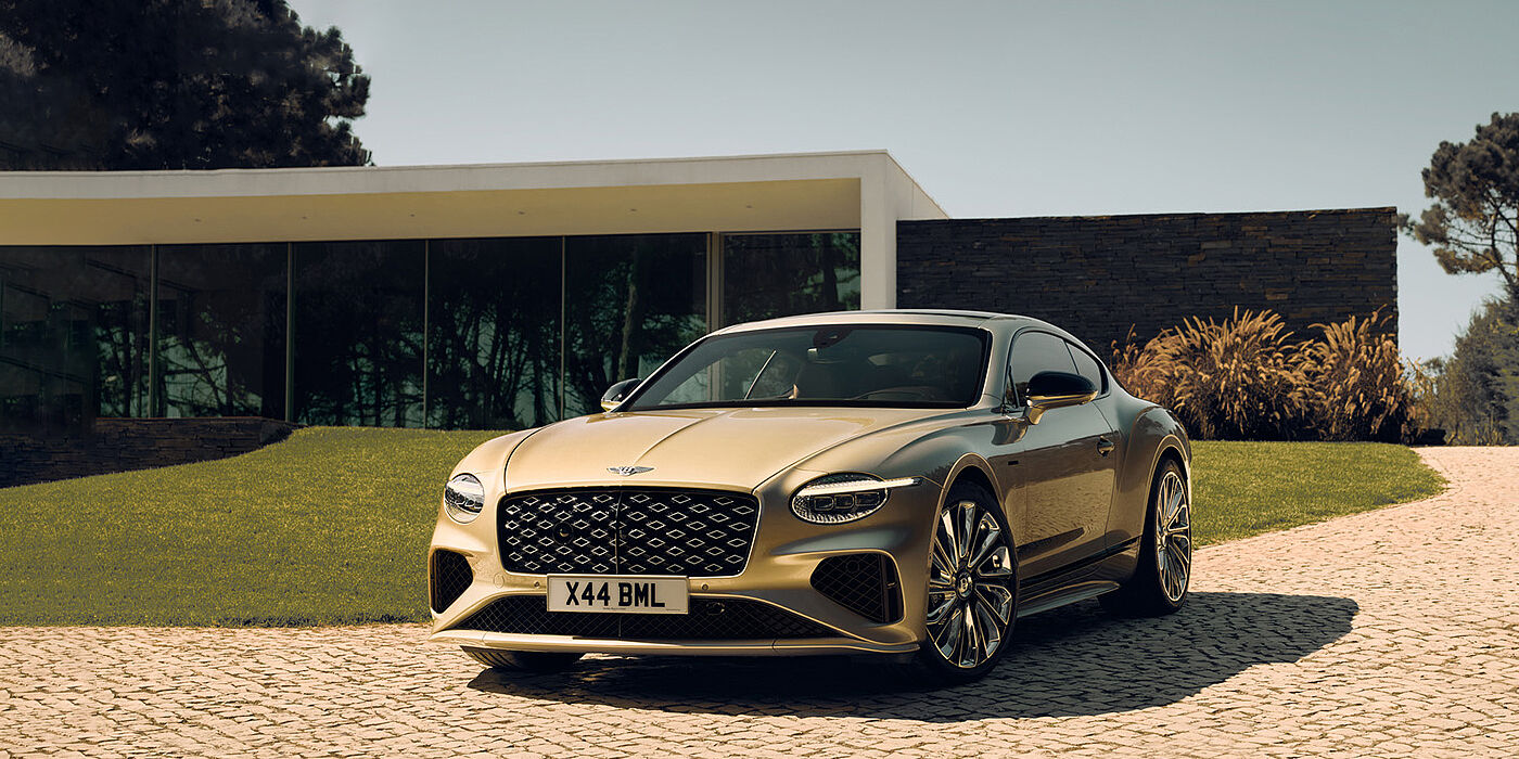 Bentley Manchester Bentley Continental GT Mulliner coupe front three quarters in Patina paint parked outside a glass fronted building with a grass lawn behind it