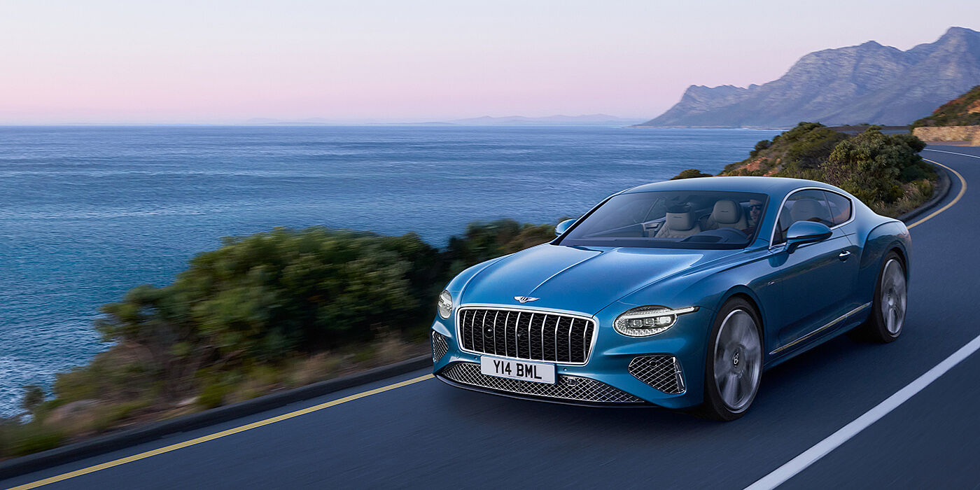 Bentley Manchester New Bentley Continental GT Azure coupe in Light Windsor blue paint with 22 inch Azure wheels and chrome grill, driving dynamically by the sea