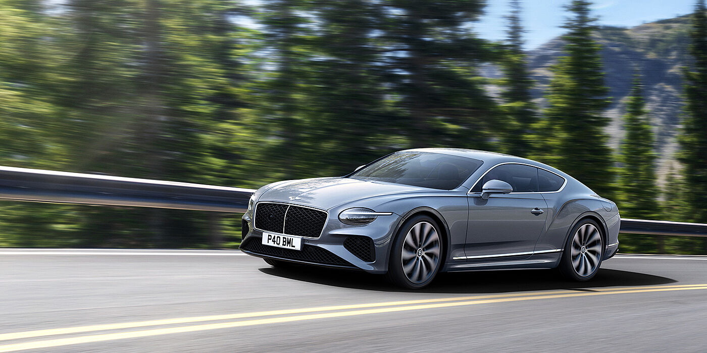 Bentley Manchester New Bentley Continental GT coupe in Silverlake paint and 22 inch ten-spoke wheels, driving dynamically on a tree-lined road in the sunshine