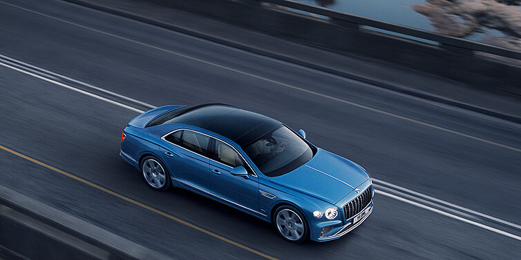 Bentley Manchester New Bentley Flying Spur Azure sedan in Light windsor blue paint by Mulliner, with 22 inch Azure wheels seen from overhead driving dynamically on a country road