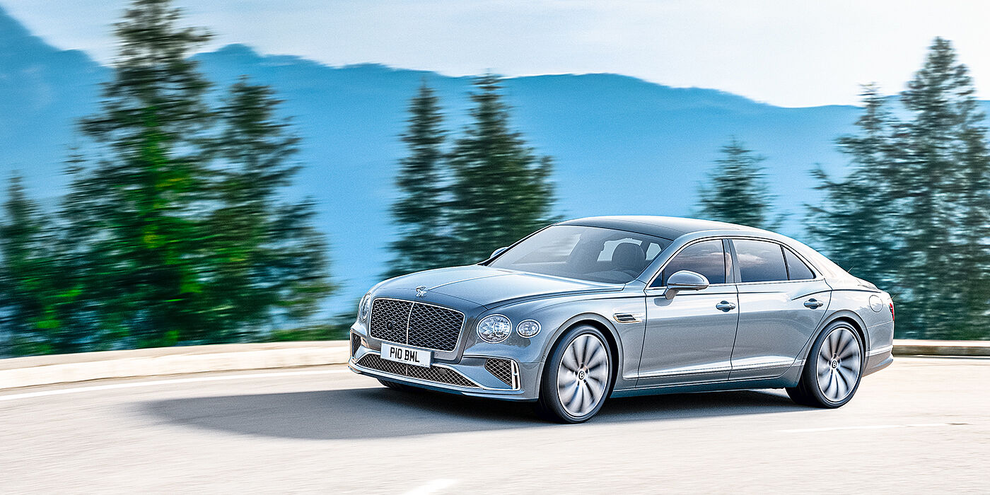 Bentley Manchester New Bentley Flying Spur sedan side view in Silverlake paint with ten spoke wheels and chrome matrix grille driving dynamically on a mountain road