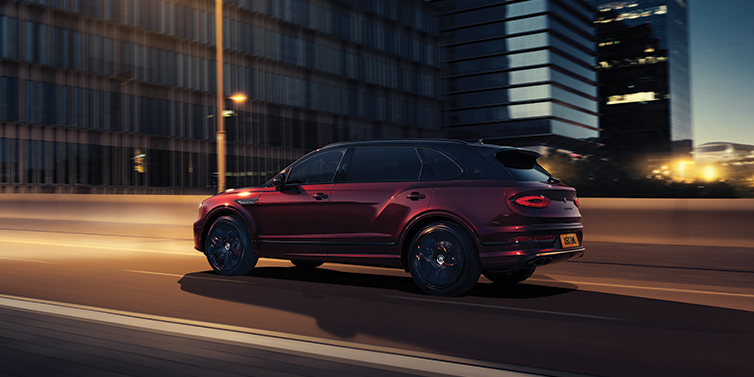 Bentley Manchester Bentley Bentayga Extended Wheelbase Mulliner SUV in Cricket Ball red paint driving dynamically in city at night